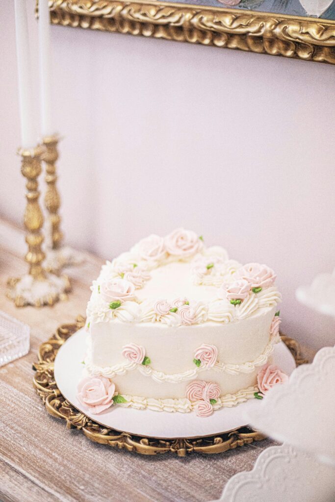 A beautifully lit Barbie cake display on a sleek, modern table with a white marble surface. The Barbie doll, dressed in a flowing pink gown, emerges gracefully from the center of the cake, surrounded by delicate buttercream frosting rosettes and shimmering edible glitter. Soft, directional lighting highlights the intricate cake details and the Barbie's elegant pose. The overall scene exudes a sense of sophistication and celebration, perfectly capturing the essence of "Presenting Your Finished Barbie Cake".